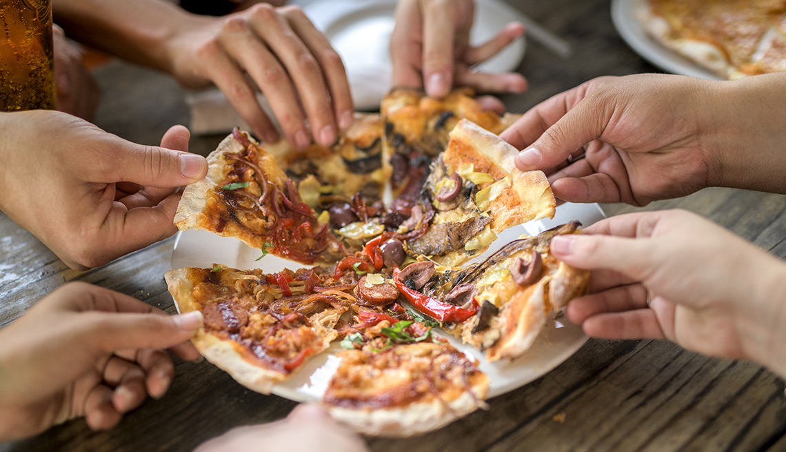 A cropped image showing the hands of a group of friends taking a slice of pizza at a table