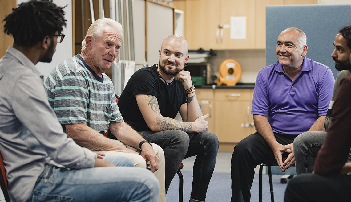 Diverse group of men are talking and laughing together in an alcoholism support group.