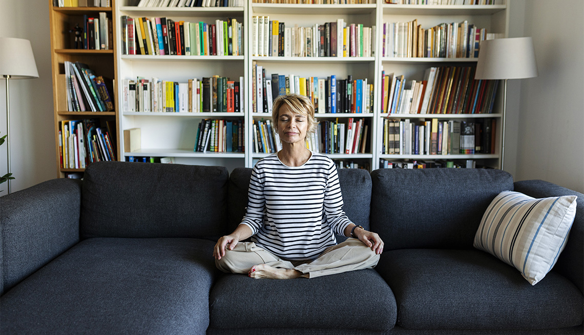 Mature woman practicing yoga on couch at home