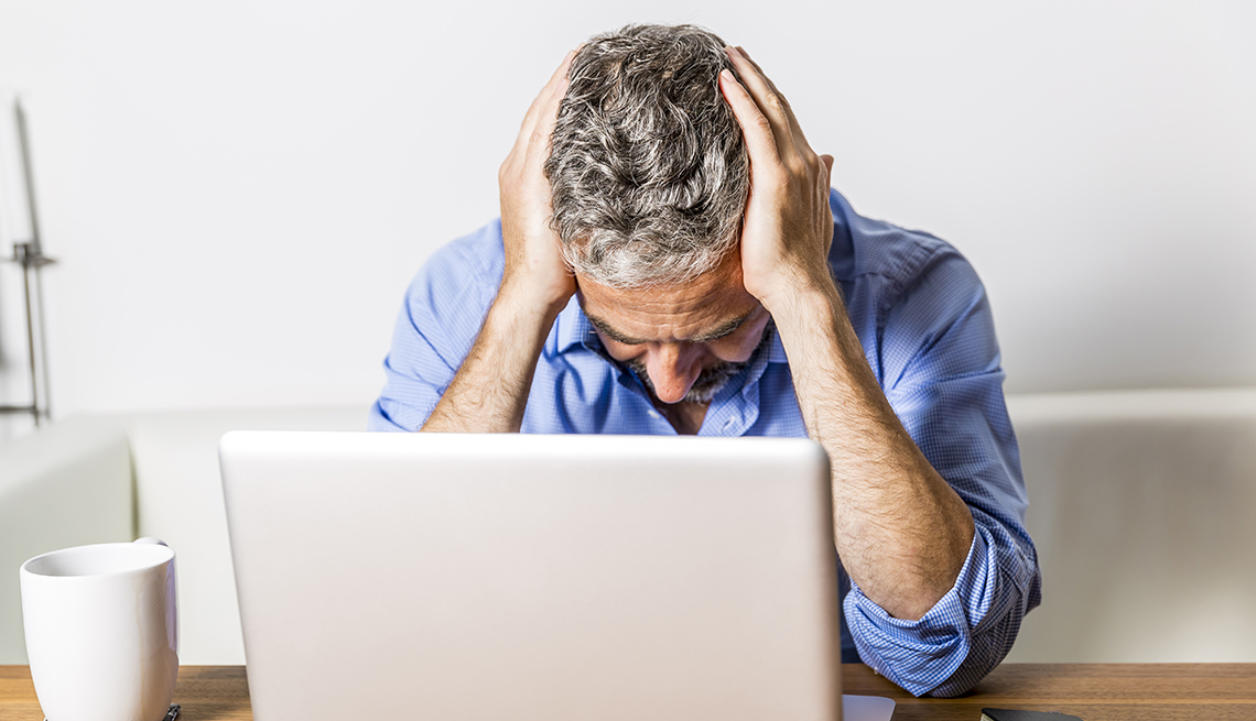 frustrated man holds his head while looking at computer in his home office