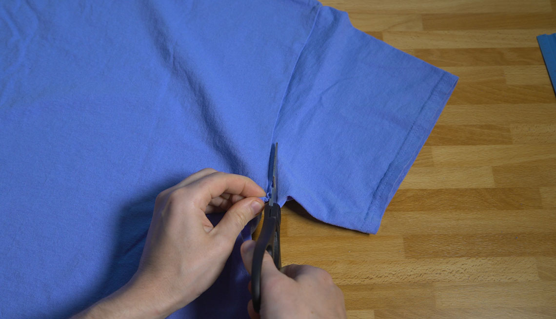 Cutting a sleeve off a cotton t-shirt with scissors.