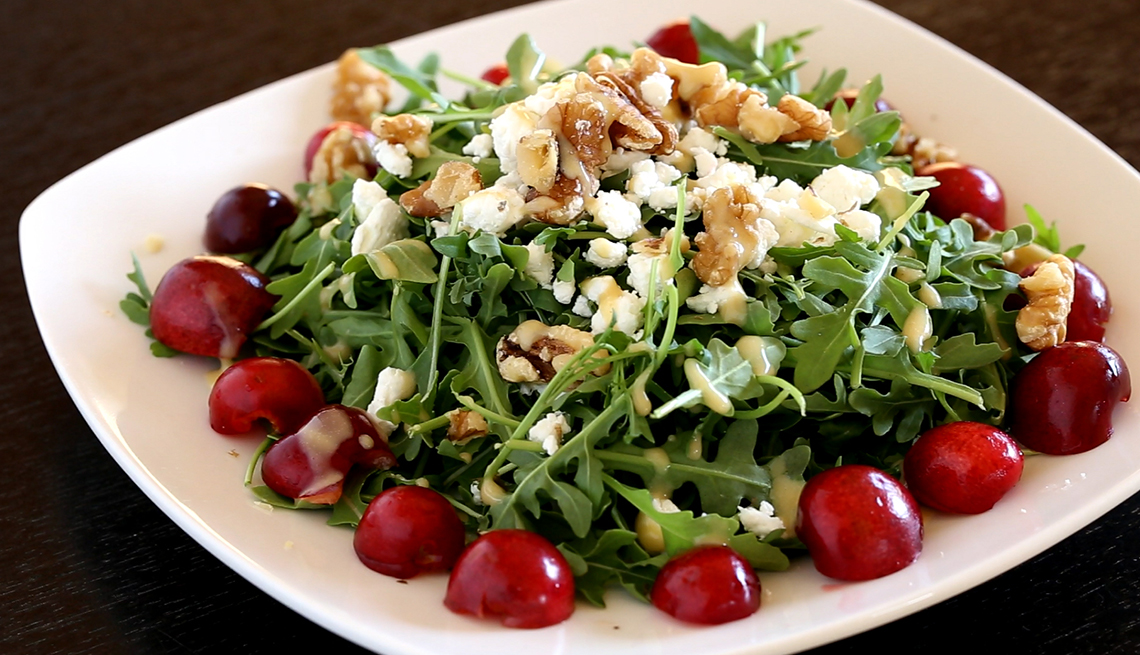 plate of arugula lettuce salad with sliced cherries goat cheese and nuts