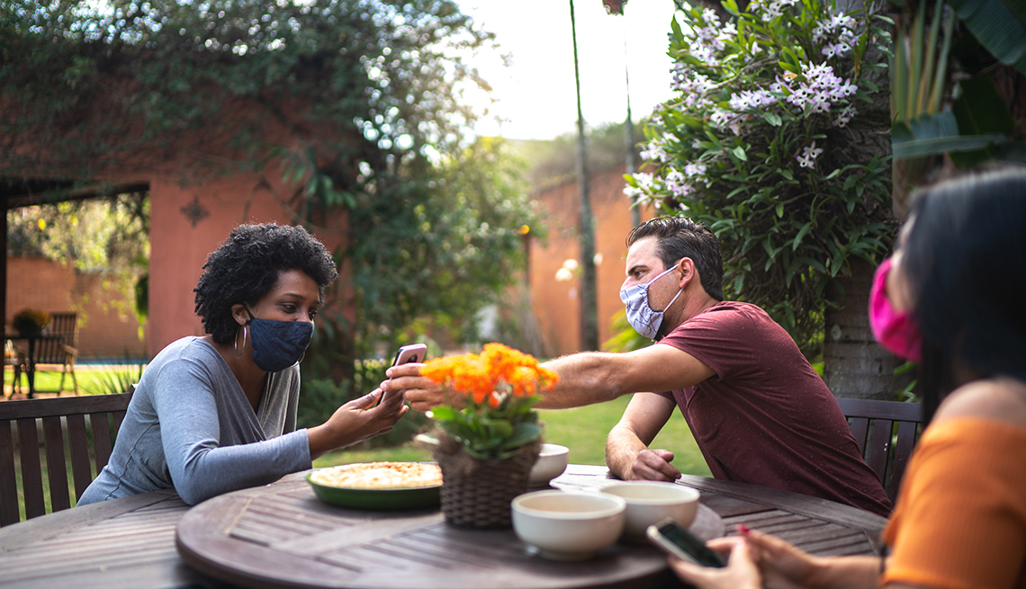 Friends reunited in the backyard, talking and using smartphone while wearing face masks