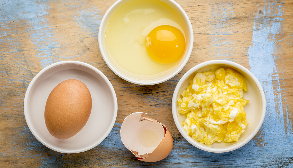 white bowls with scrambled and raw eggs on a wood table