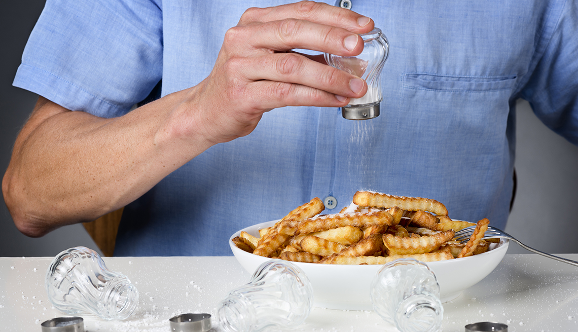 Una persona le pone sal a unas papas fritas y sobre la mesa varios frascos de sal vacíos