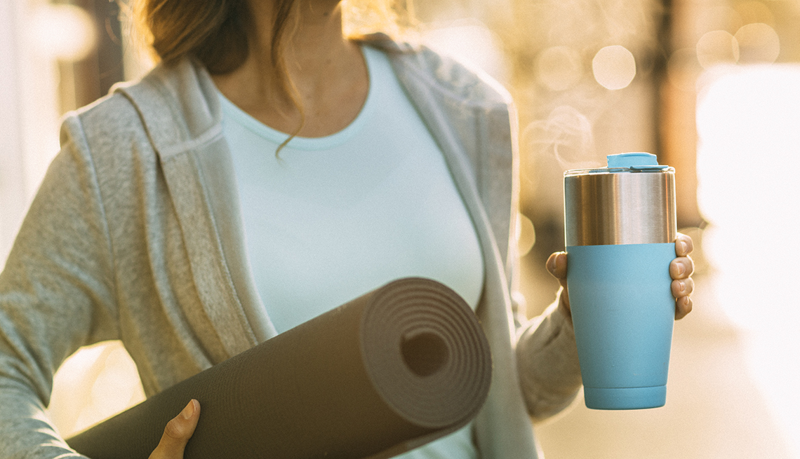 Una mujer con un colchón de yoga y una taza de café