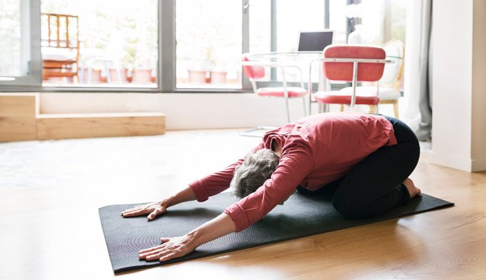woman crouched on her knees on the ground with her arms extended in front of her while on a yoga mat