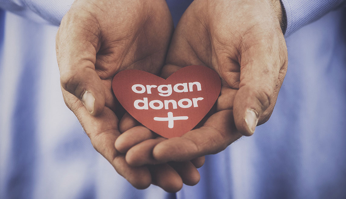 Manos juntas sostienen un corazón de papel que dice donante de órganos