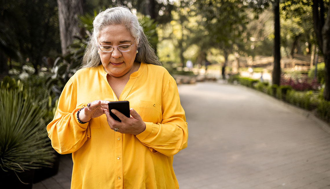 Una mujer mayor caminando por el parque usando su celular.