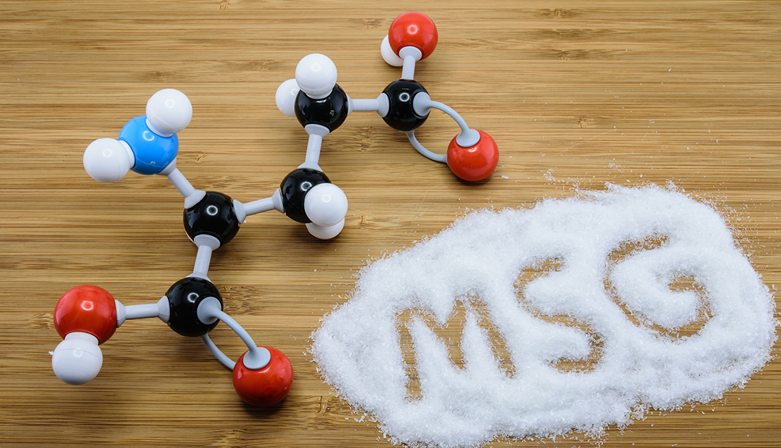 Estructuras moleculares del glutamato monosódico sobre una mesa donde hay azúcar derramada y las letras MSG escritas en el azúcar