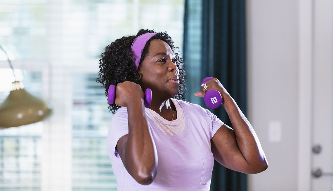 a woman in a purple shirt and headband lifts matching purple two-pound dumbbells in her living room