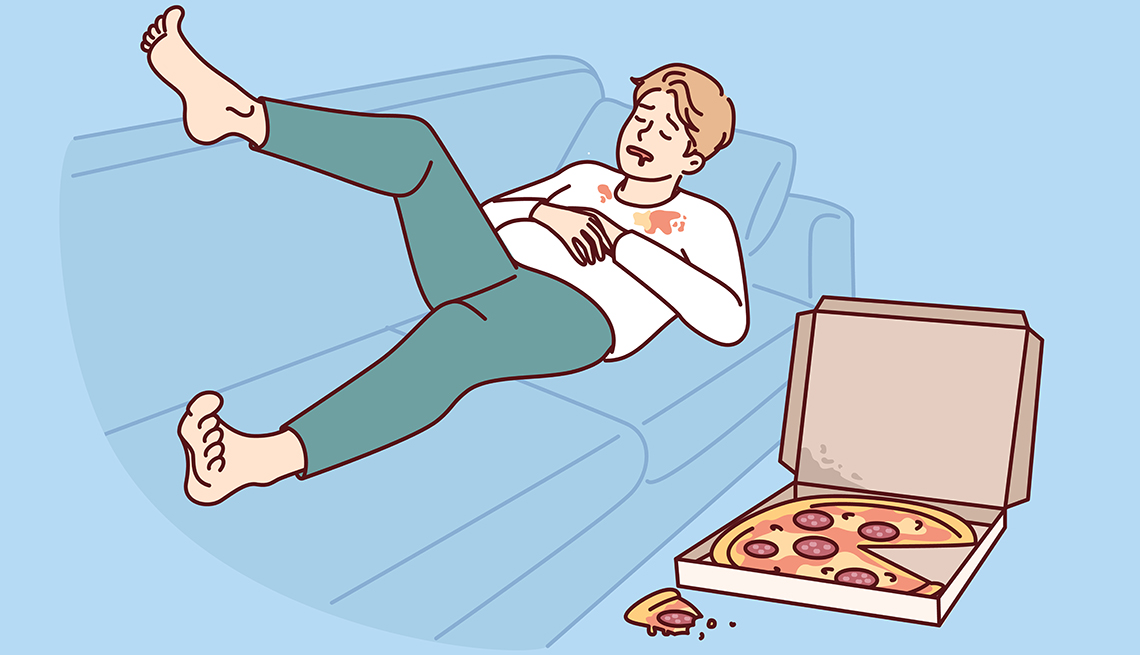 Ilustración de un hombre acostado en un sofá que sostiene su estómago después de haber comido una pizza que tiene al lado.
