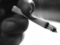Hand holding burning cigarette - CT scans reduce risk of lung cancer deaths for current and former smokers.