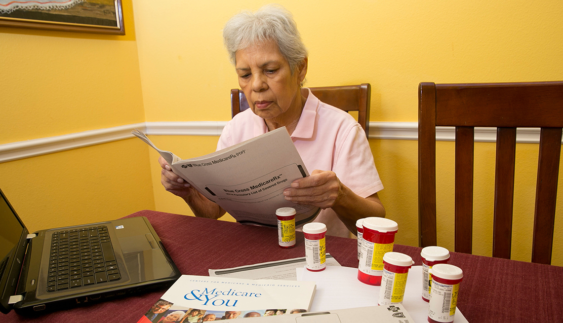 Mujer mayor leyendo un documento y varios frascos de medicinas sobre una mesa