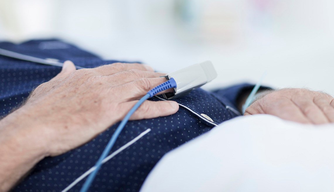 A close-up view of an mature male patient's hands. He is laying in a hospital bed.