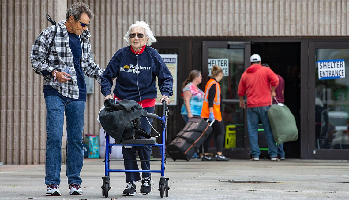 Man helping a woman using a walker outside of a shelter