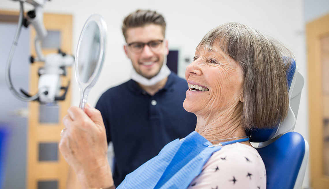 Una paciente se mira sus dientes en un espejo mientras la observa su dentista