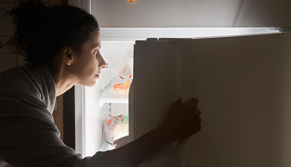 Mujer abriendo un refrigerador de noche - Cómo el insomnio puede llevar a comer en exceso