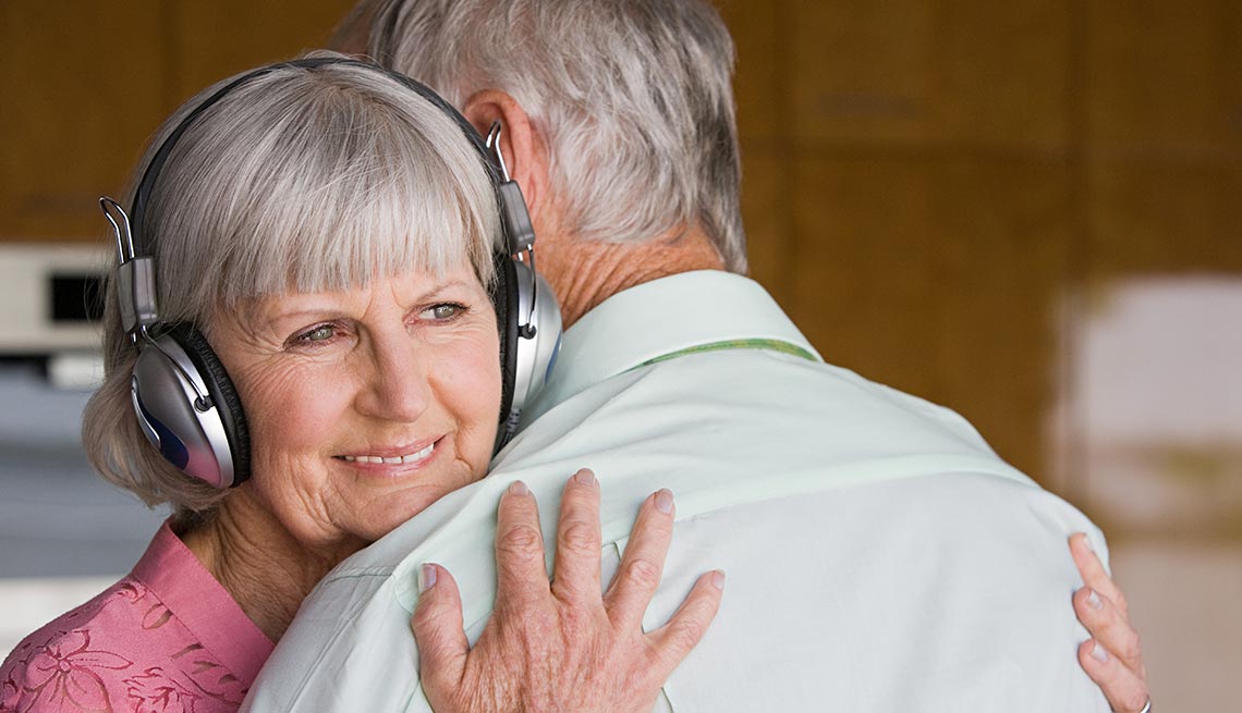 Mujer mayor con audífonos abraza a un hombre - La importancia de los aparatos auditivos en el cuidado