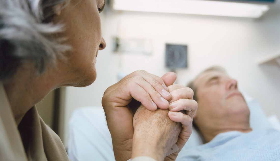 Mujer sostiene la mano de un hombre que está en el hospital - La alimentación artificial al final de la vida