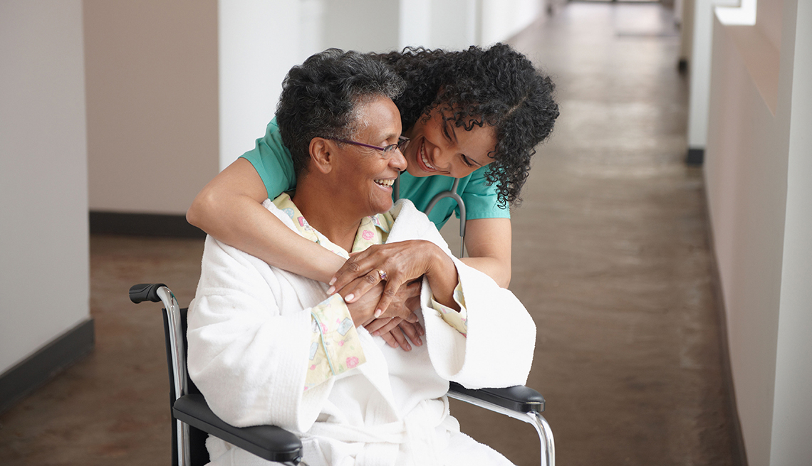 Enfermera abraza y se ríe con una mujer adulta sentada en una silla de ruedas