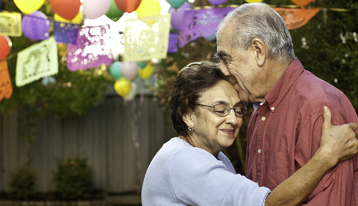 Hombre y mujer mayores, abrazados en una celebración en el patio de una casa.