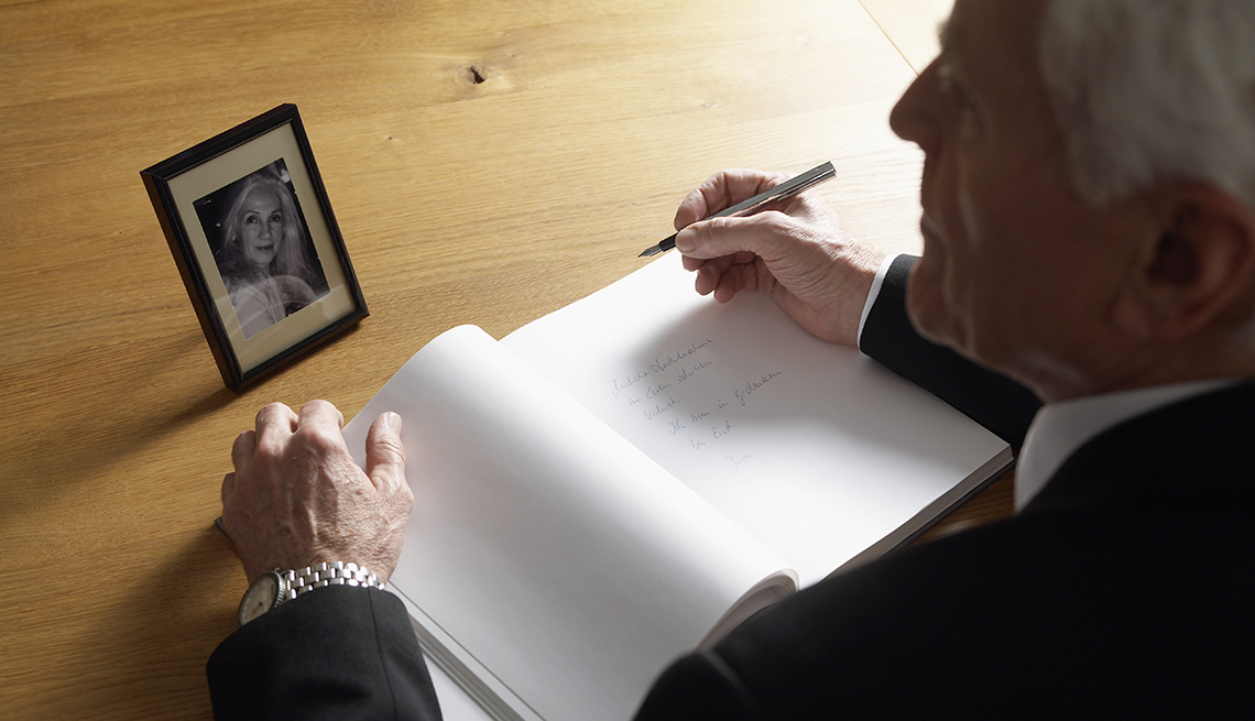 man sitting at a desk with a pen and notepad writing a eulogy while looking at a picture of his late wife