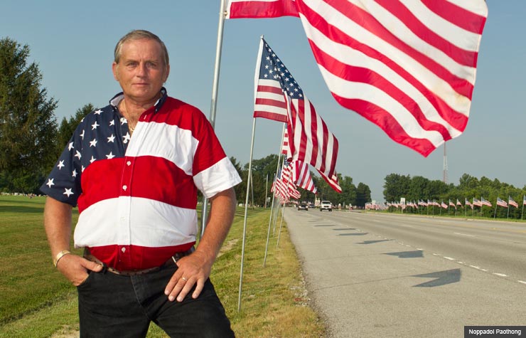 Larry Eckhardt, 54 of Little York, IL, stands next to American flags.