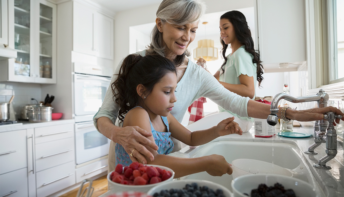 Marcar la diferencia de generación en generación - Mujer mayor sonríe mientras está en la cocina con dos niñas