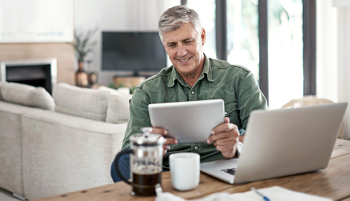 Hombre mayor usando una tableta electrónica y un computador en la mesa de su casa