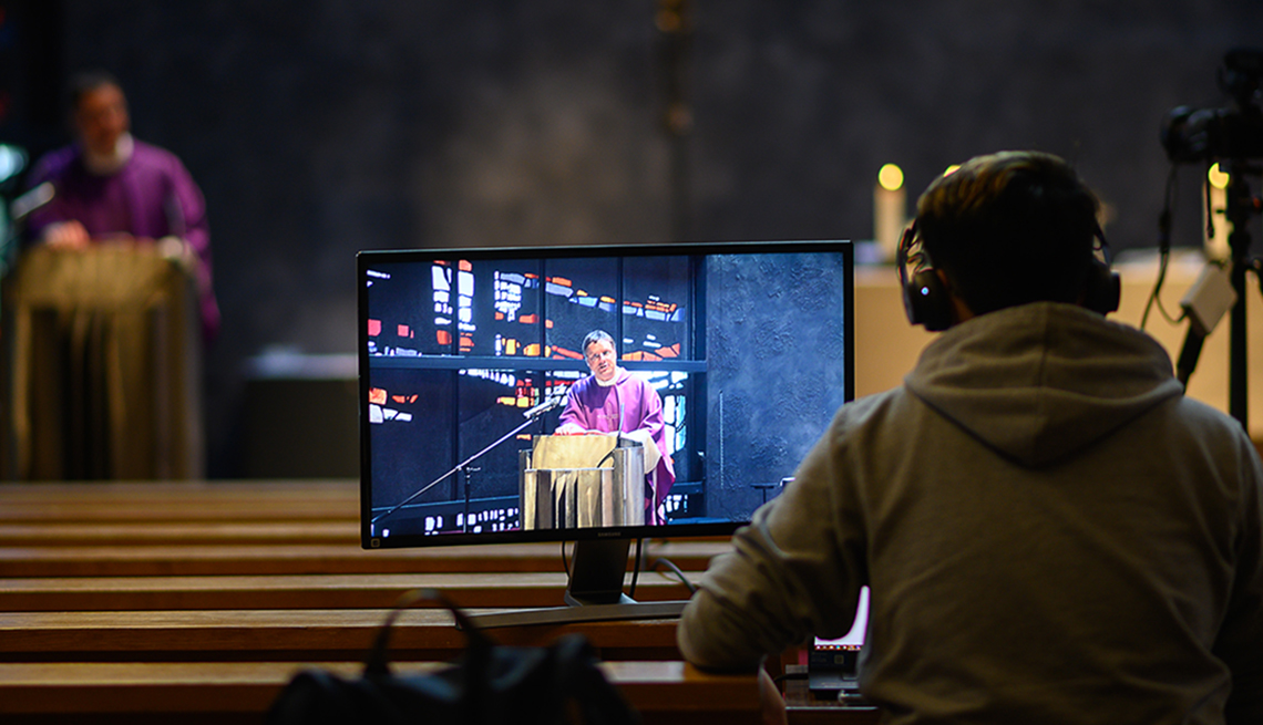 A man sitting in a church behind a computer screen wearing headphones as he records the service to live stream
