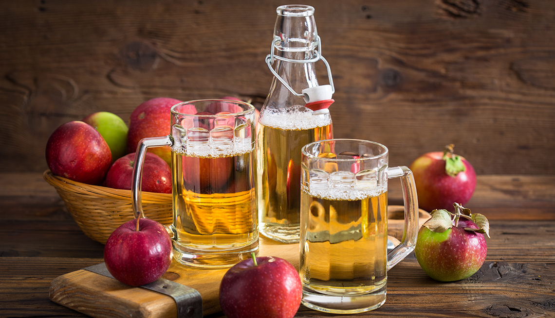 Sidra de manzana en jarras de cerveza rodeadas de manzanas sobre un fondo de madera