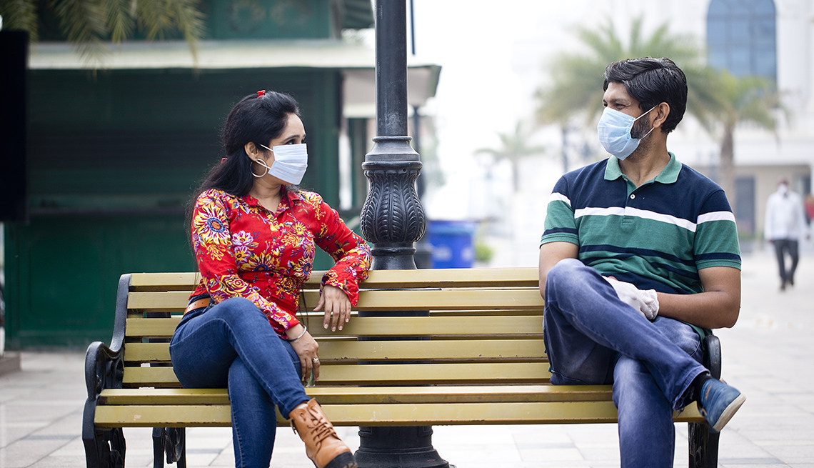 Una mujer y un hombre con máscaras sentados en una silla del parque