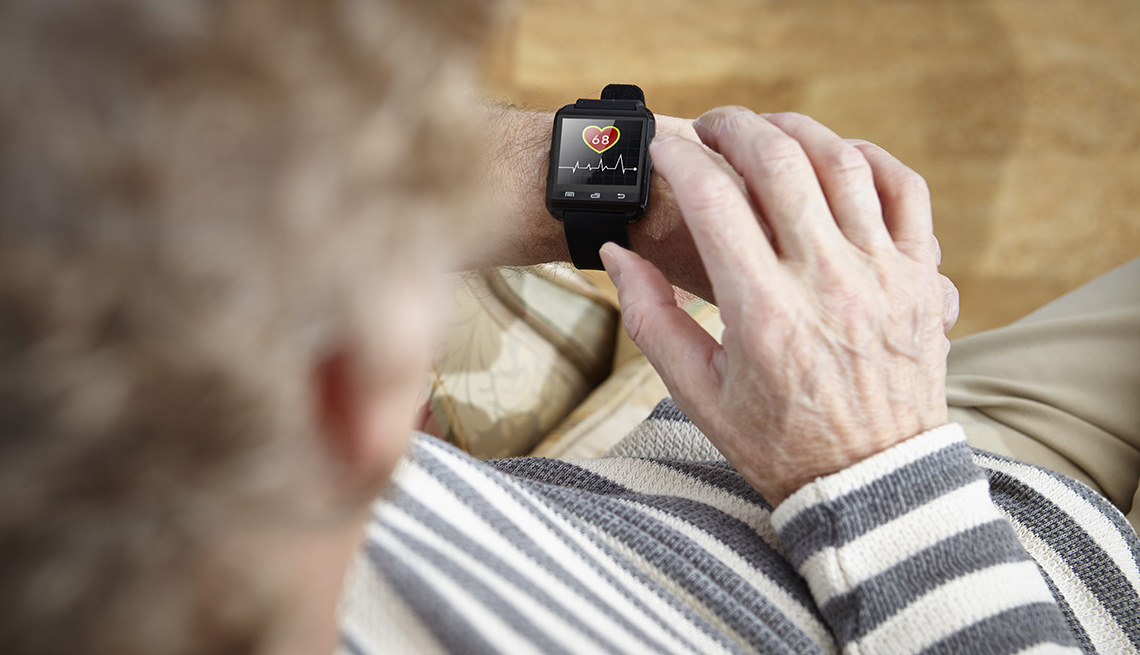 Un hombre mayor sentado en un sillón observa su reloj inteligente o smartwatch