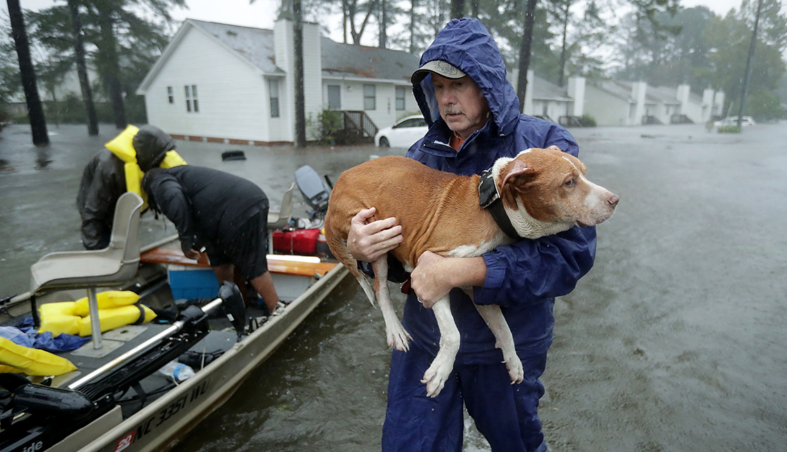 Un hombre sostiene una mascota en una calle inundada con un pequeño bote cerca