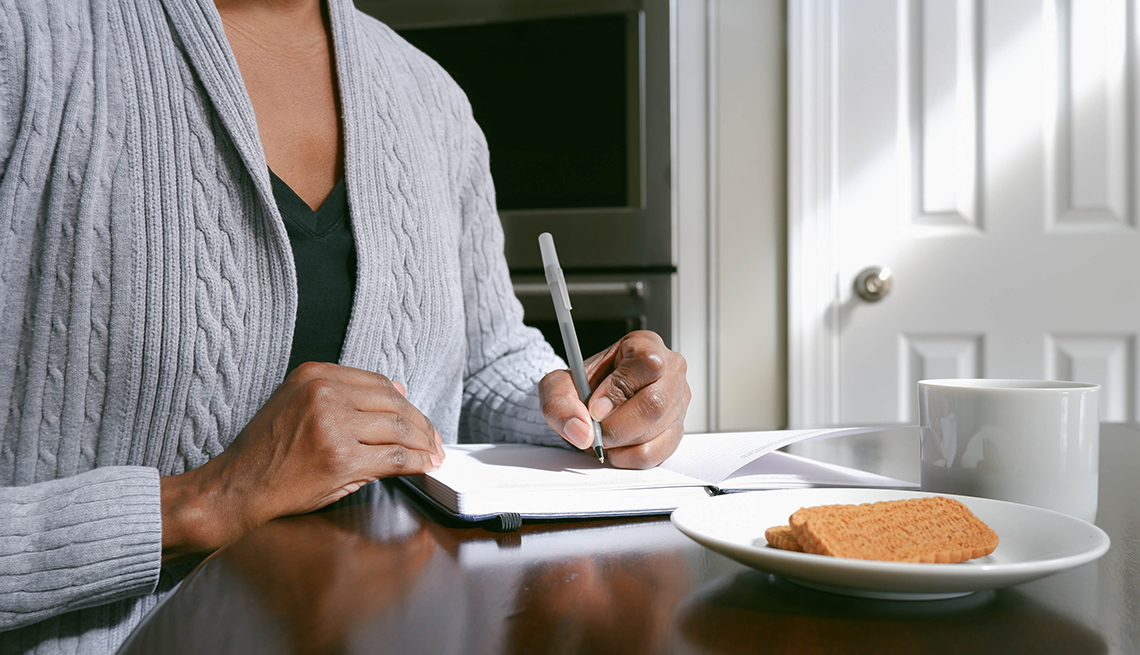 Close-up of unrecognizable woman writing in journal at kitchen table