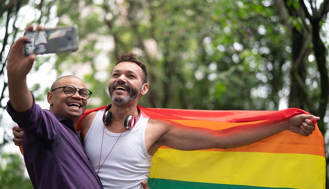 Dos hombres sosteniendo una bandera del arco iris, tomando una foto