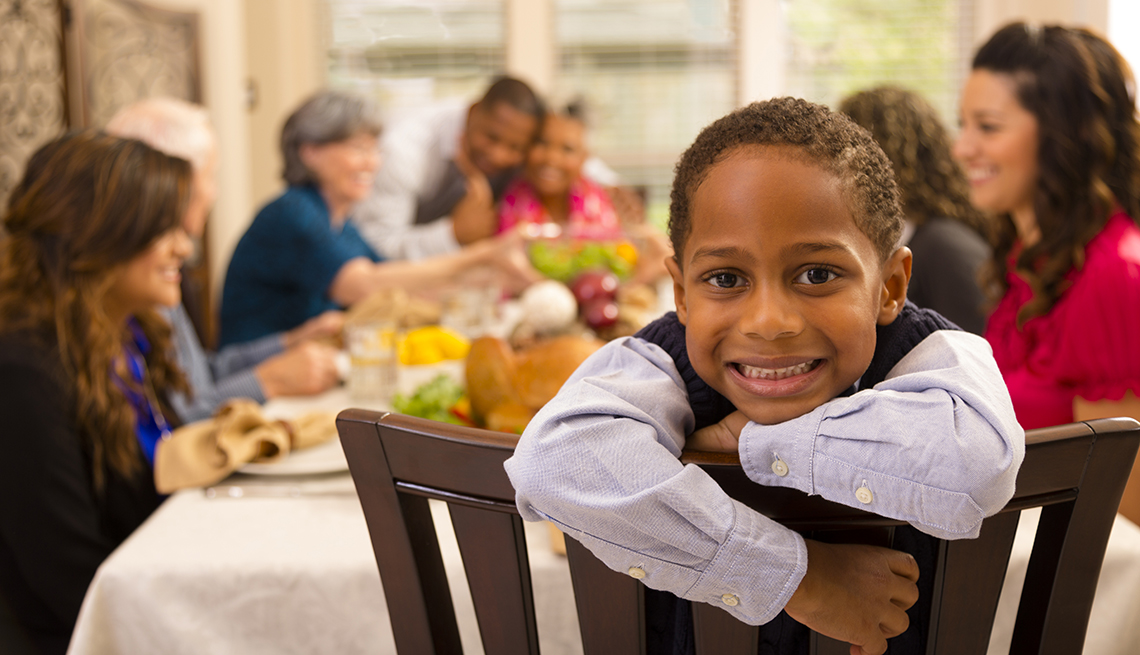 a little boy turned around in his chair at the thanksgiving family table smiles at the camera
