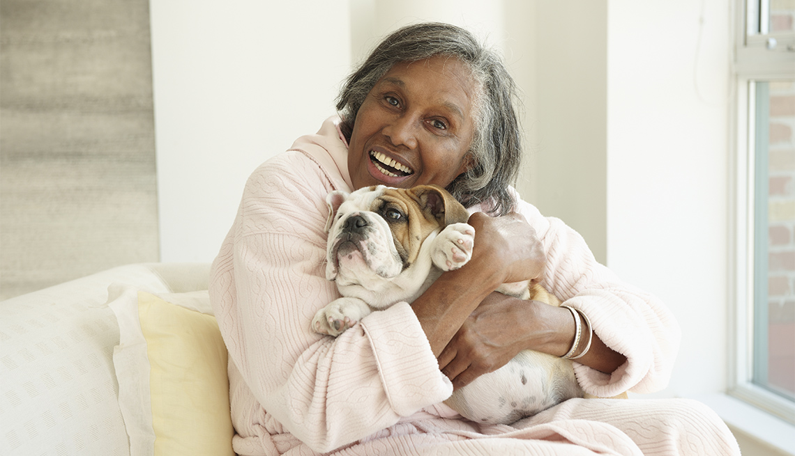 woman sitting on a couch, hugs pet bull dog 