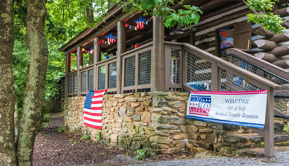 log cabin in a wooded area with july fourth decorations and a sign saying welcome fourth of july annual family reunion