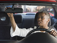 Mujer afroamericana mirando a su espejo retrovisor - Seguridad de los automóviles: una guía para compradores
