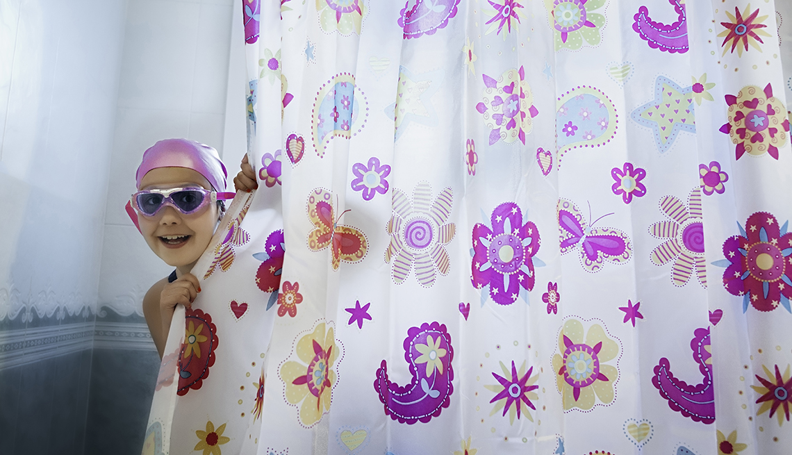 Niño con gorro y gafas de natación asomándose detrás de una cortina baño colorida.