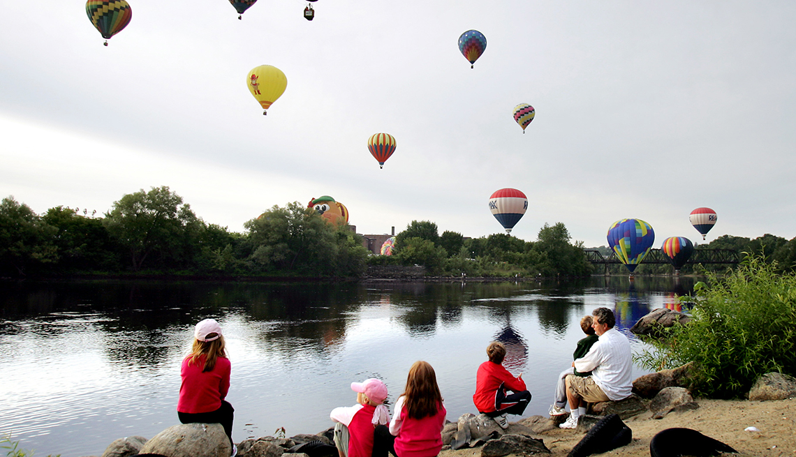 Family watches hot air balloons in the air by a river.