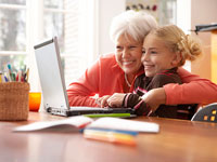 Grandmother embracing her granddaughter as she uses a laptop computer - How to keep your computer safe for children