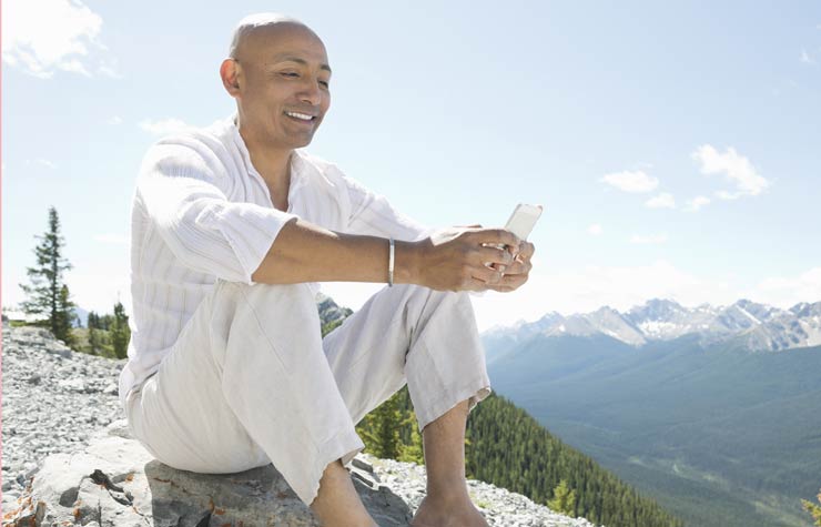 Hombre sonriendo con un teléfono inteligente en cima de una montaña, Consejos de teléfonos inteligentes para los Viajeros