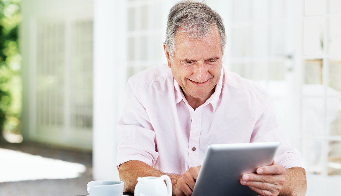 Un hombre mayor sonriente trabaja en una tableta digital.