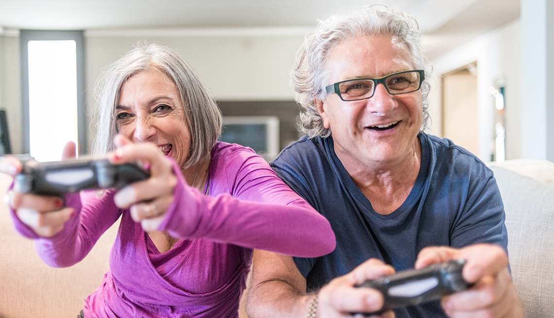 Pareja de abuelos sentados felices en el sofá con controles de videojuegos en sus manos
