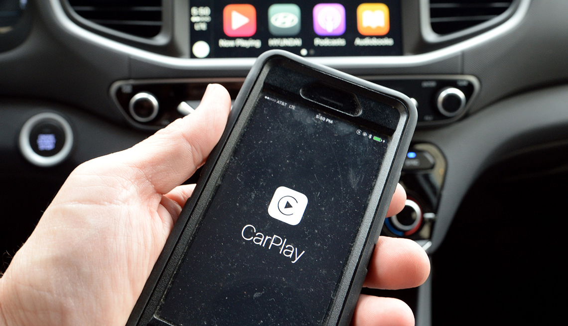 a hand holding a smartphone with the carplay app on it in front of a dashboard