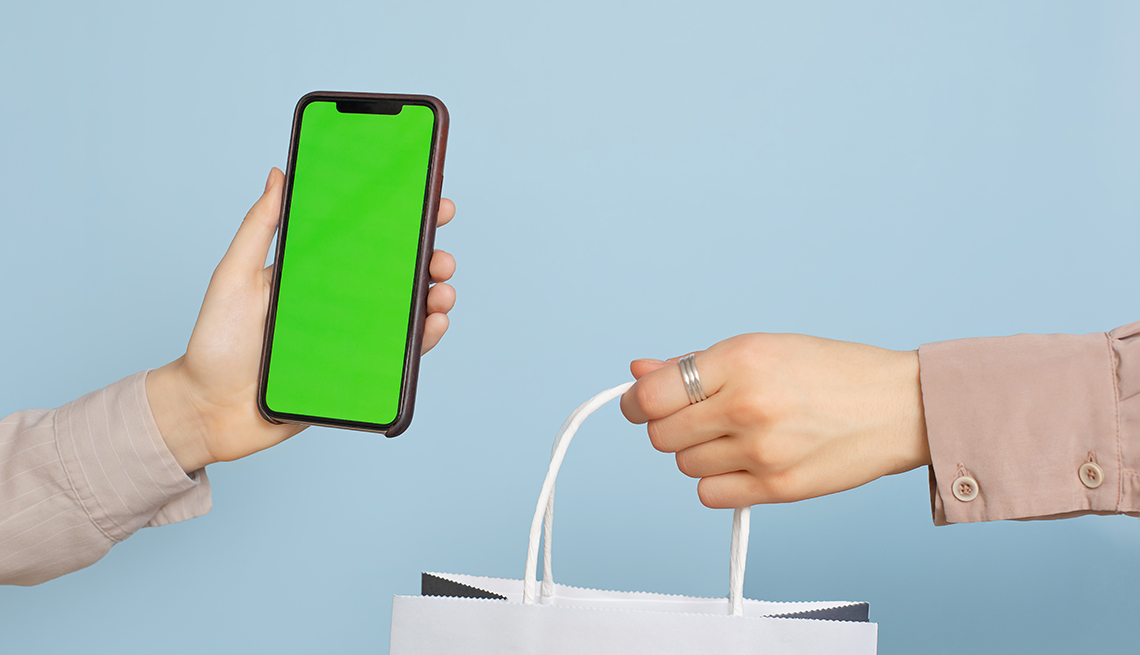 one hand holding a generic smartphone and another holding a shopping bag