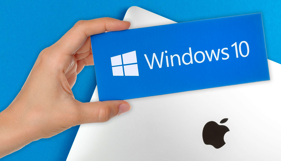hand holding a box that says windows 10 with the microsoft logo above a macbook laptop